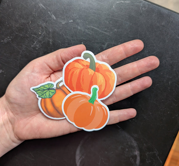 Hand holding a paper cutout of two pumpkins on a black surface
